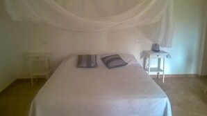 Una habitación sencilla y limpia con una cama, dos almohadas, una mesita de noche y una lámpara.
