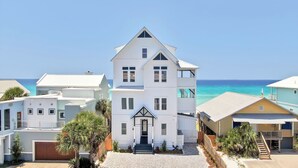 A white two-story building with a balcony, a staircase leading to the entrance, and a view of the ocean.