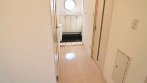 A narrow hallway with a bathroom at the end, featuring a round mirror, white cabinets, and a tiled floor.