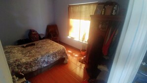 A bedroom with a bed, a wardrobe, a window with curtains, and a small table with a plant.