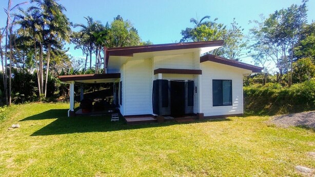 A modern two-story house with a covered porch, surrounded by lush greenery and tall trees.