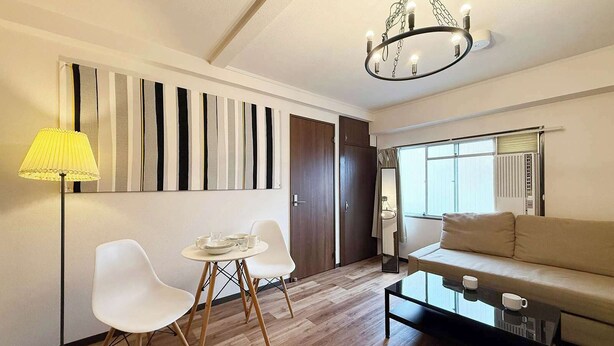 A modern living room with a sofa, two white chairs, a coffee table, a lamp, and a chandelier. - 1 Bedrm Apt 5mins from Hiroshima Sta  5ppl (302) (Hiroshima City)