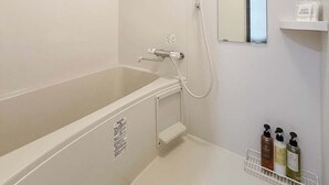 A modern bathroom with a bathtub, a shower, a mirror, and a shelf with toiletries. - 1 Bedrm Apt 5mins from Hiroshima Sta  5ppl (302) (Hiroshima City)