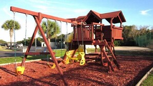 A wooden swing set with a slide and climbing structure, surrounded by mulch. - Summerhouse 228 (St. Augustine)