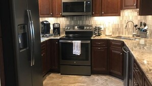 A kitchen with dark wooden cabinets, a stainless steel refrigerator, a microwave, an oven, and a dishwasher. - Summerhouse 101 (St. Augustine)