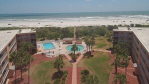 Un hôtel doté de deux piscines, offrant une vue sur la plage et comprenant un jardin aménagé avec des palmiers.