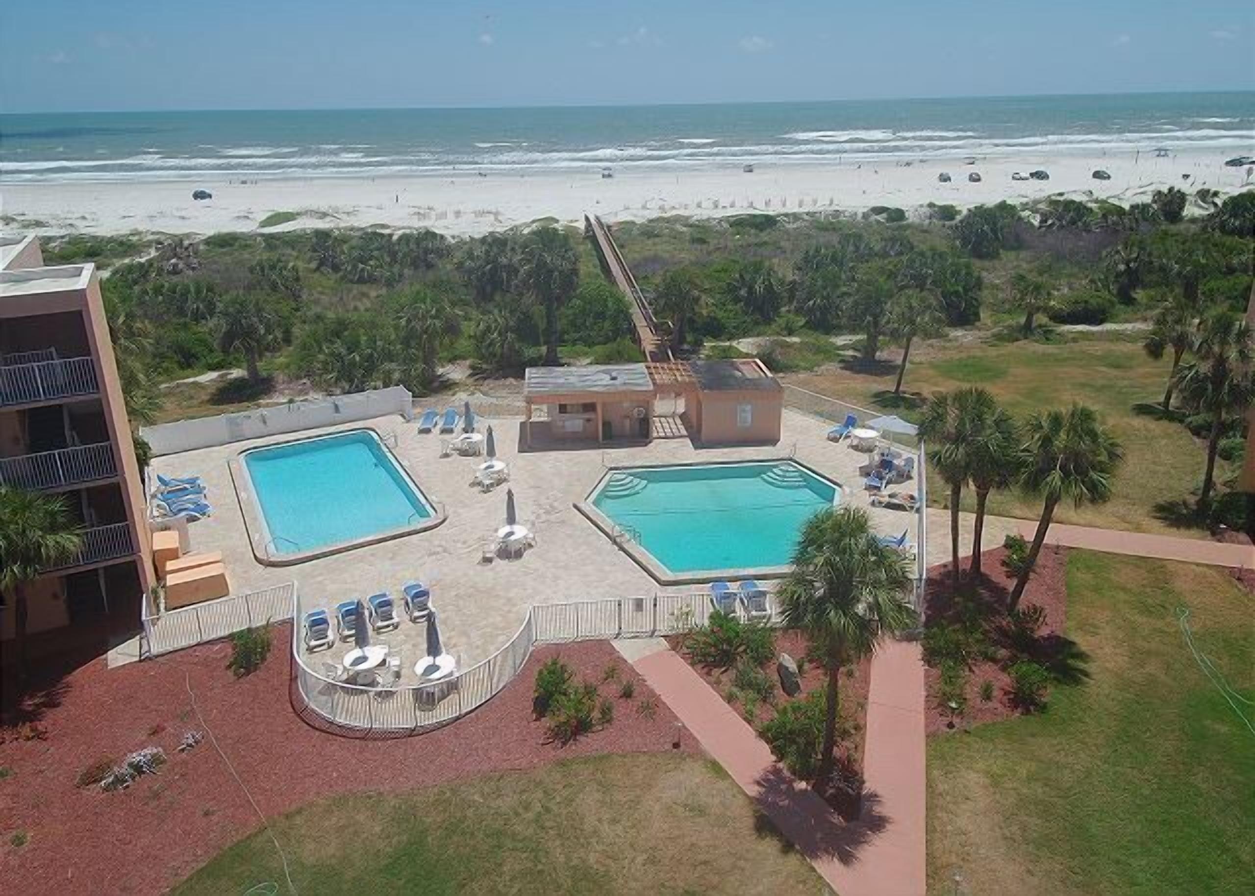 A resort with two swimming pools, a beach view, and a parking area.