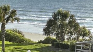 A view of the ocean from a window overlooking a grassy area with palm trees and a bench. - Summerhouse 251 (St. Augustine)