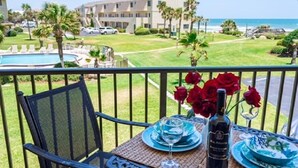 A balcony with a table set for two, overlooking a pool and a building with a view of the ocean. - Summerhouse 251 (St. Augustine)