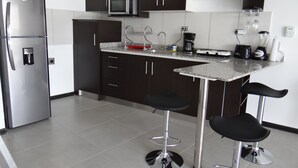 A modern kitchen with dark cabinets, stainless steel appliances, a granite countertop, and two bar stools. - Beautiful Apartment in Alajuela downtown 5 (Alajuela)