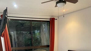 A bedroom with a bed, a window with curtains, a ceiling fan, and a view of greenery outside. - Beautiful Apartment in Alajuela downtown 5 (Alajuela)