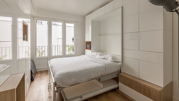 Une chambre moderne avec un lit, une armoire intégrée et de grandes fenêtres.