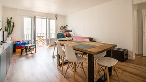 Un vaste espace de vie comprenant une table à manger en bois, des chaises blanches et un balcon avec vue.