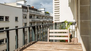 Un balcon doté d’une table en bois, d’une rambarde en métal et offrant une vue sur les bâtiments voisins.