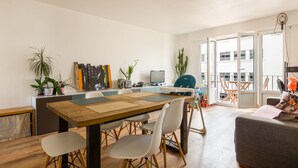 Un salon moderne avec une table à manger en bois, des chaises blanches et un canapé gris.