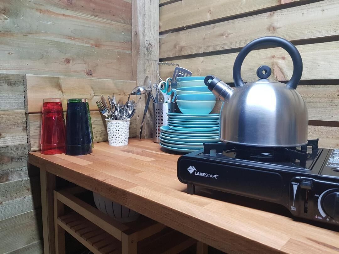 A wooden table with a portable gas stove, a kettle, and stacked blue plates.