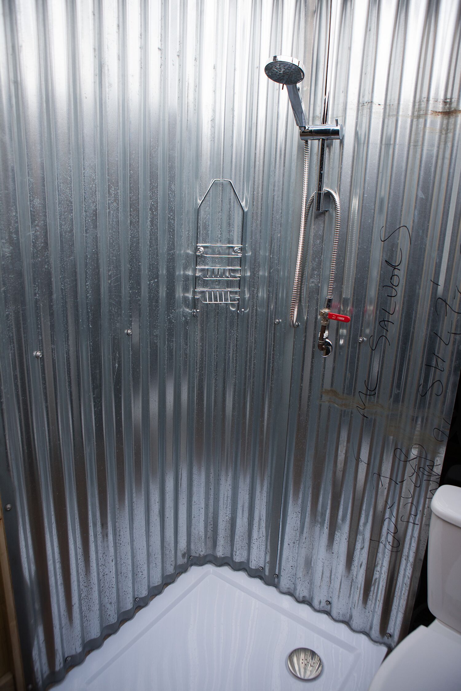 A small, enclosed shower area with a metal wall, a showerhead, and a toilet.