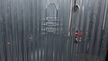 A small, enclosed shower area with a metal wall, a showerhead, and a toilet.