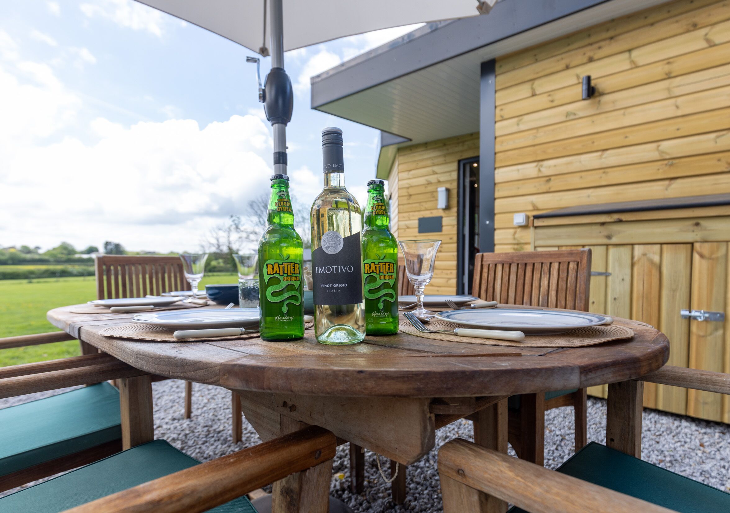A wooden table set outdoors with bottles of Rätters beer, a glass, and a plate.