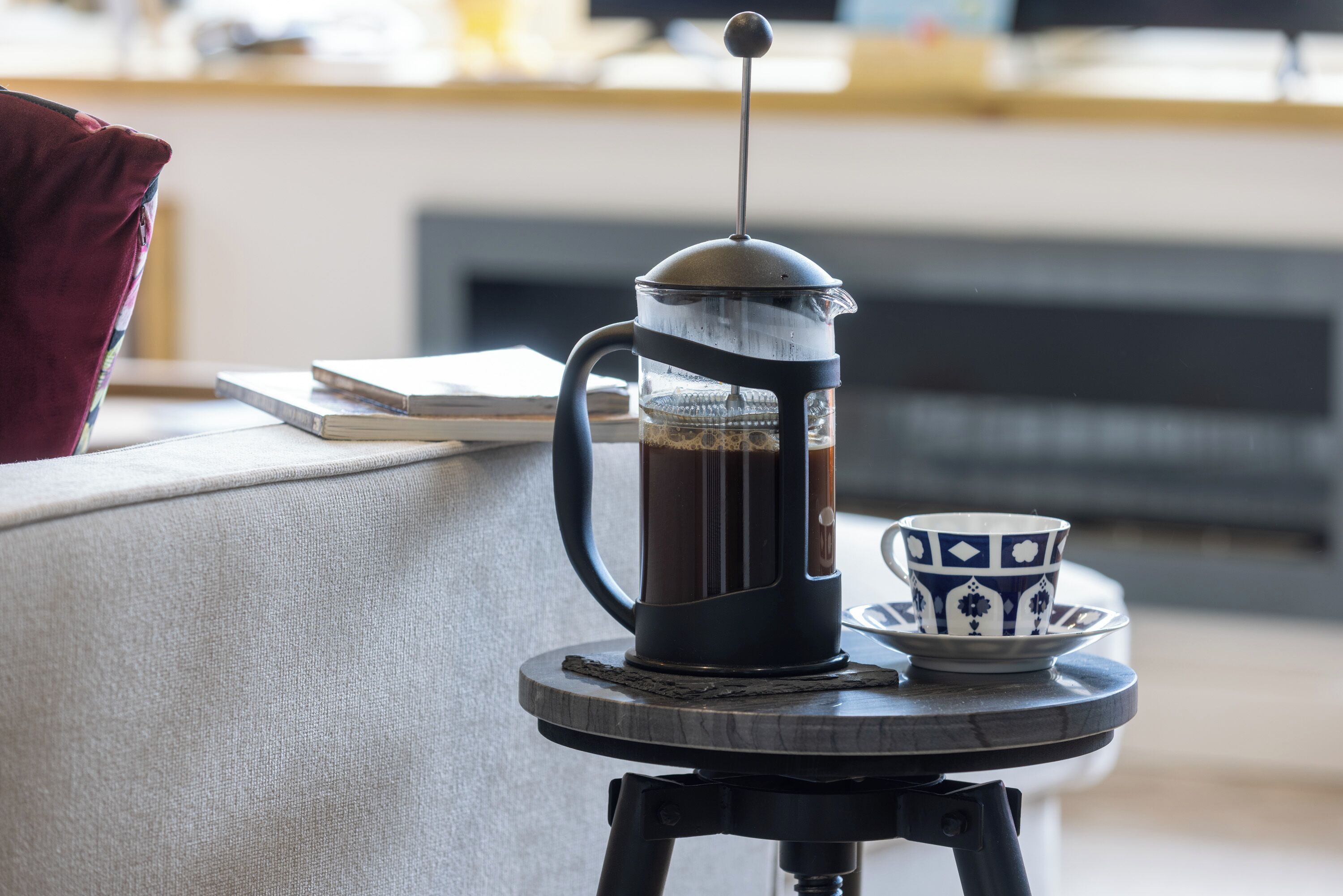 A coffee maker on a small table with a cup beside it.