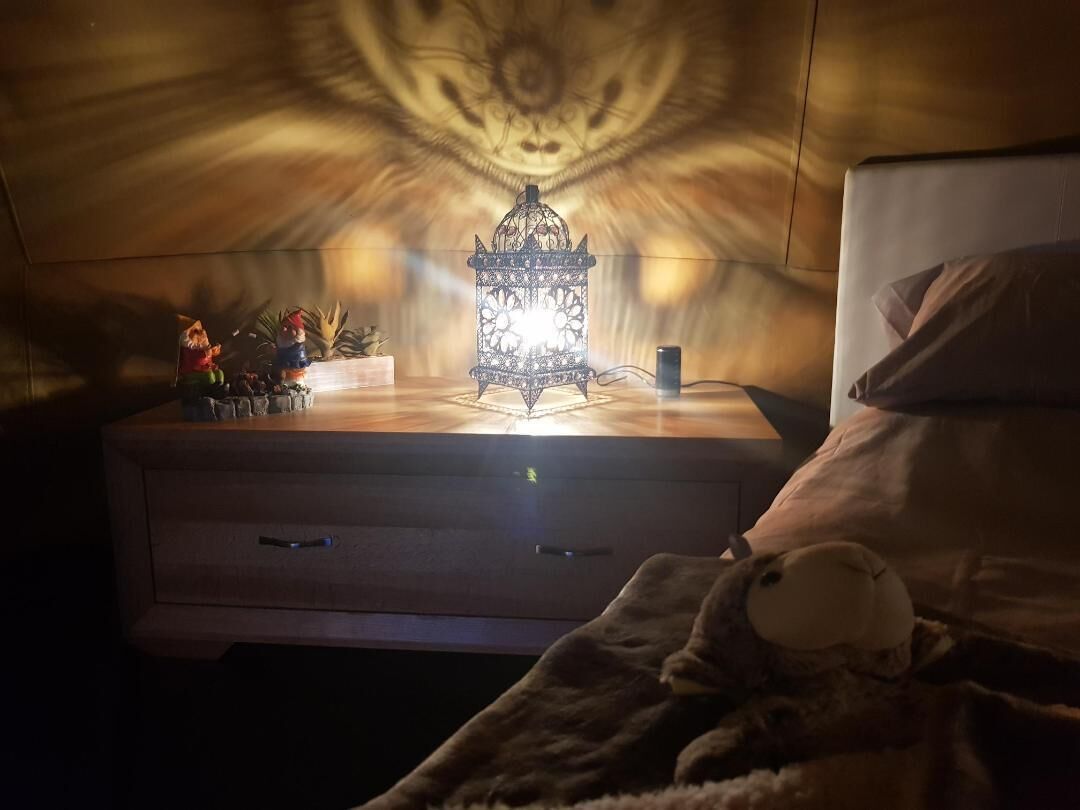 A bedroom with a nightstand, a decorative lantern, and a plush toy on the bed.