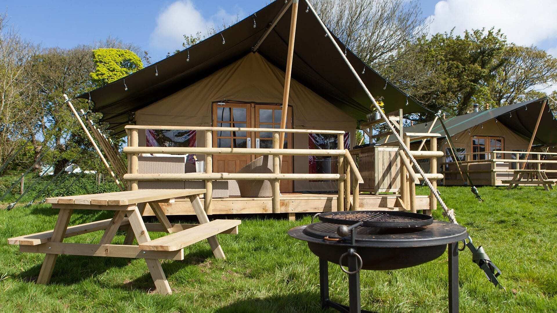 A campsite with a wooden picnic table, a grill, and a tent.