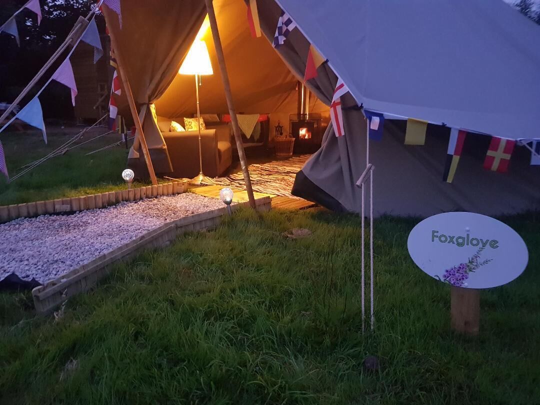 Una carpa acogedora con un interior cálido, un pozo de fuego y un letrero con el nombre 'Foxglove'.