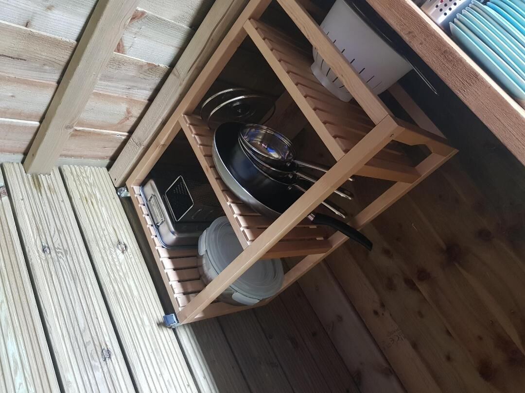 Egy fából készült polcrendszer, rajta edényekkel és egy fehér tárolóedénnyel.