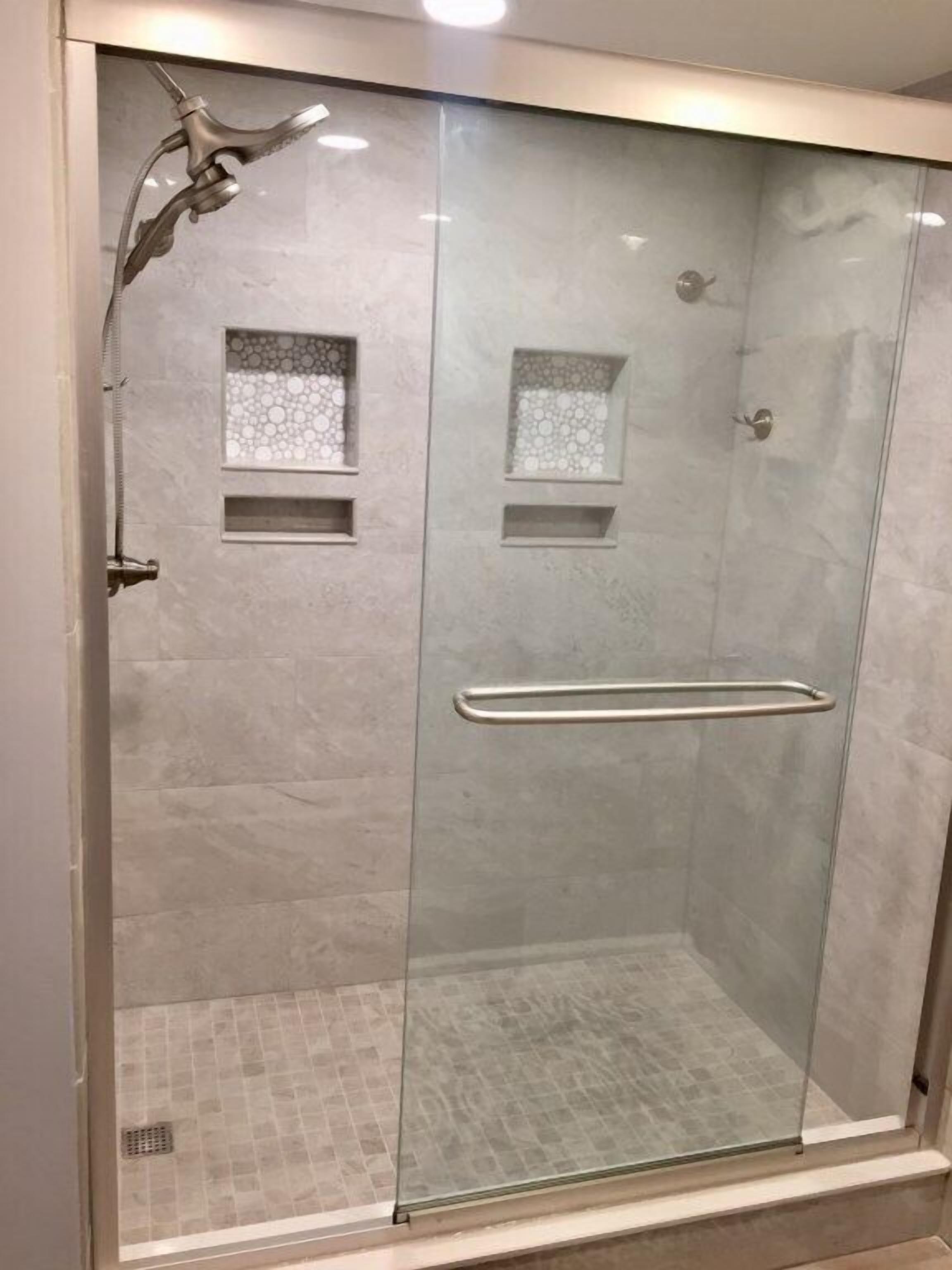 Une douche fermée par des parois en verre, dotée d’une poignée en métal et d’un pommeau de douche.