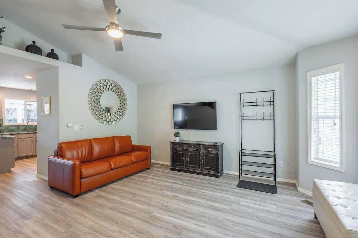 A living room with a brown leather sofa, a TV on the wall, a black metal rack, and a ceiling fan.