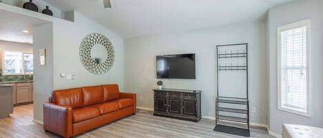A living room with a brown leather sofa, a TV on the wall, a black metal rack, and a ceiling fan.