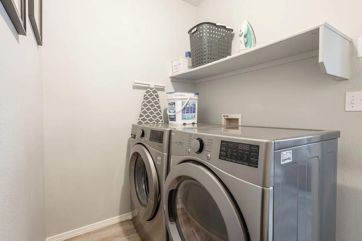 A laundry area with two front-loading washing machines, a drying machine, and a shelf with laundry supplies.