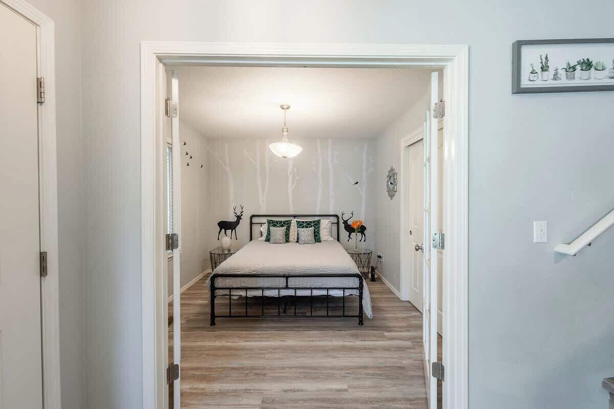 A bedroom with a bed centered in the room, a door on the left, and a staircase leading to another level.