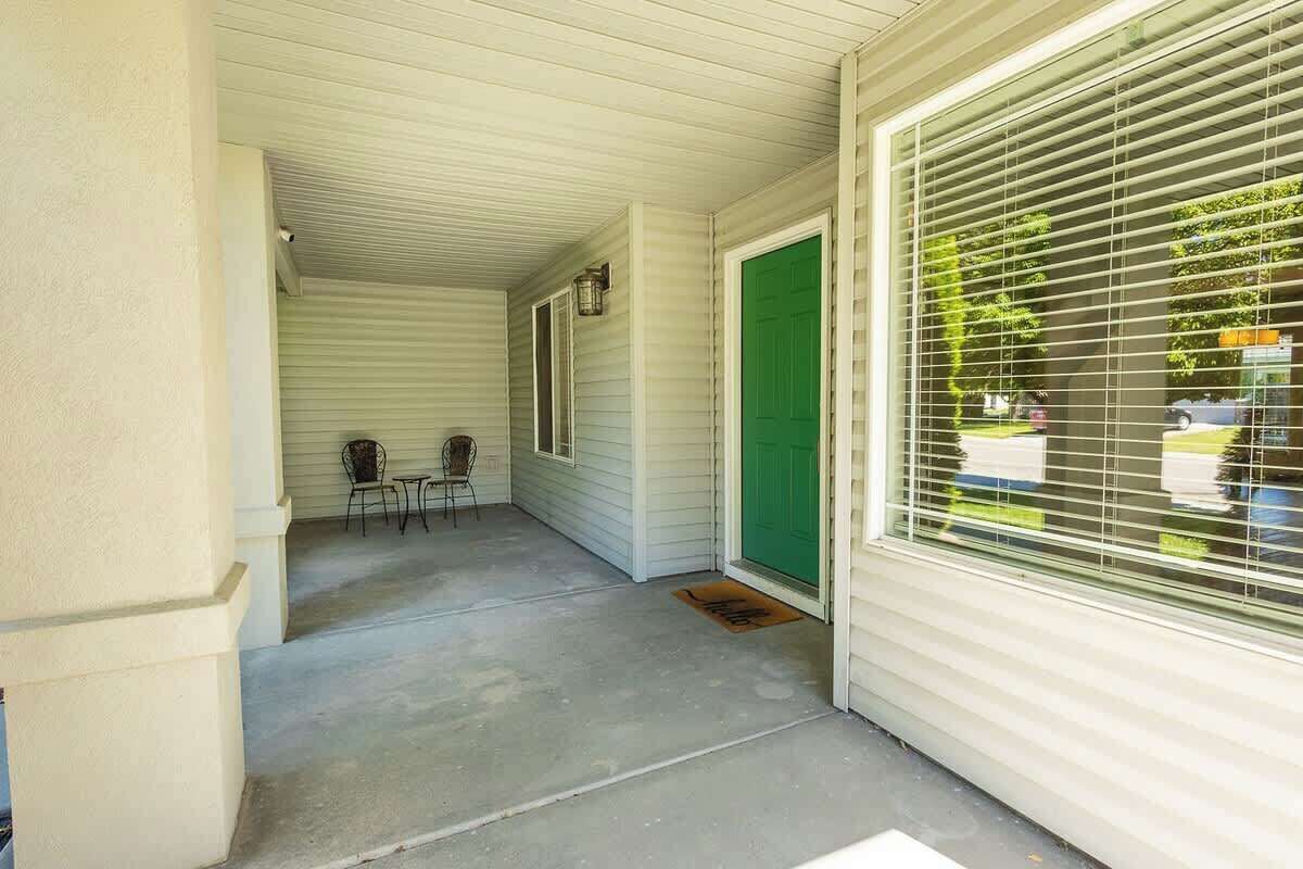 A covered porch with a concrete floor, a green door, and a window with blinds.