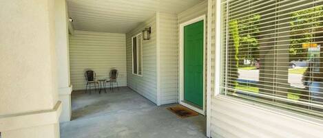 A covered porch with a concrete floor, a green door, and a window with blinds.