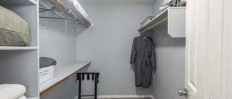 A narrow walk-in closet with shelves, a bench, and a hanging robe rack.
