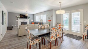 A dining area with a wooden table and floral chairs, a fireplace, and a sofa in the background. - Upscale House with Outdoor Seating/Firepit (Boise)