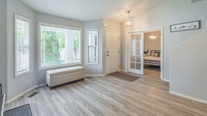 A spacious hallway with large windows, a bench, and a door leading to a bedroom. - Upscale House with Outdoor Seating/Firepit (Boise)