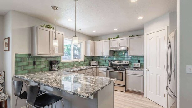 A modern kitchen with a central island, stainless steel appliances, and green backsplash tiles. - Upscale House with Outdoor Seating/Firepit (Boise)