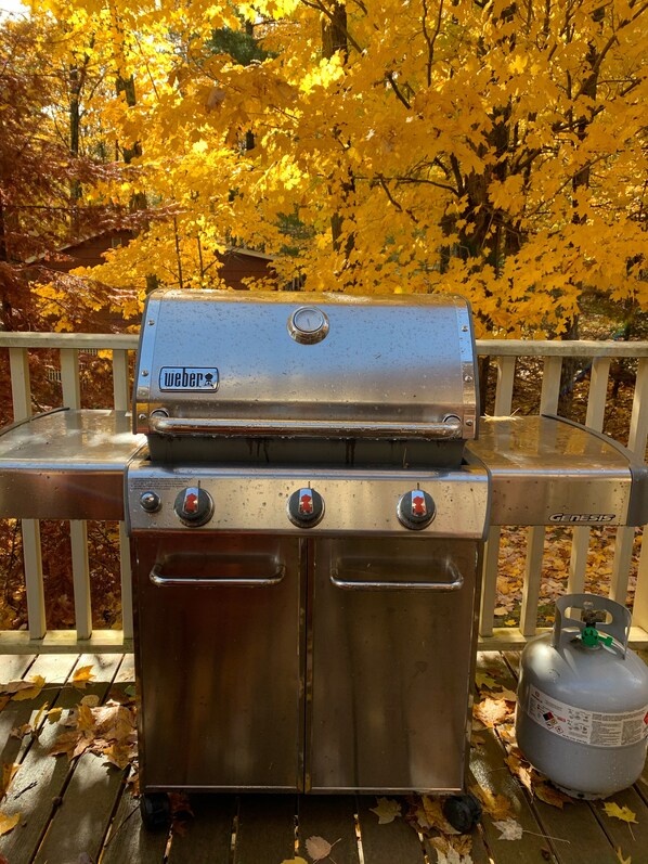 A Weber Genesis portable grill on a wooden deck with a gas tank nearby.