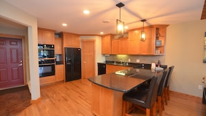 A modern kitchen with wooden cabinets, a black refrigerator, a built-in oven, a central island with bar stools, and recessed ceiling lighting. - The Landing on Lake Nebagamon - Includes Pontoon! (Lake Nebagamon)