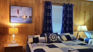 Ein Schlafzimmer mit einer holzverkleideten Wand, einem Bett mit einer maritime-Optik-Quiltdecke, einem Nachttisch mit einer Lampe und einem Gemälde eines Segelboots.