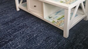 Ein Wohnzimmer mit einem weißen Couchtisch, der mit einem Landschaftsdruck versehen ist, einem Korbtisch, einer Lampe und einem Sofa mit floralen Kissen.