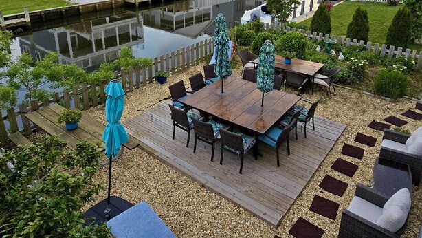 Eine Terrasse im Freien mit Holzboden, Tisch und Stühlen sowie einem blauen Sonnenschirm.