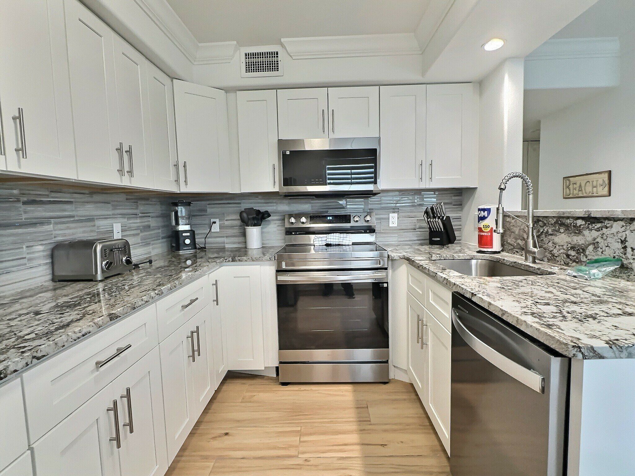 A modern kitchen with white cabinets, stainless steel appliances, and a granite countertop.