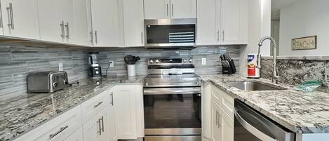 A modern kitchen with white cabinets, stainless steel appliances, and a granite countertop.