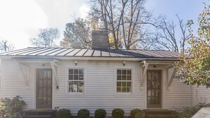 Een gelijkvloers huis met een veranda, een schoorsteen en een kleine voortuin met vormgesnoeide struiken.