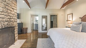 Slaapkamer met een stenen muur, houten balken, een groot bed, een nachtkastje en uitzicht op een andere kamer.