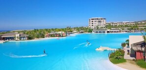 Una piscina grande y cristalina de color azul con vistas a un edificio de resort y palmeras al fondo.