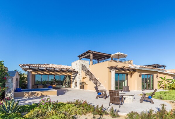 A modern house with a patio, outdoor seating, and a staircase leading to a balcony.